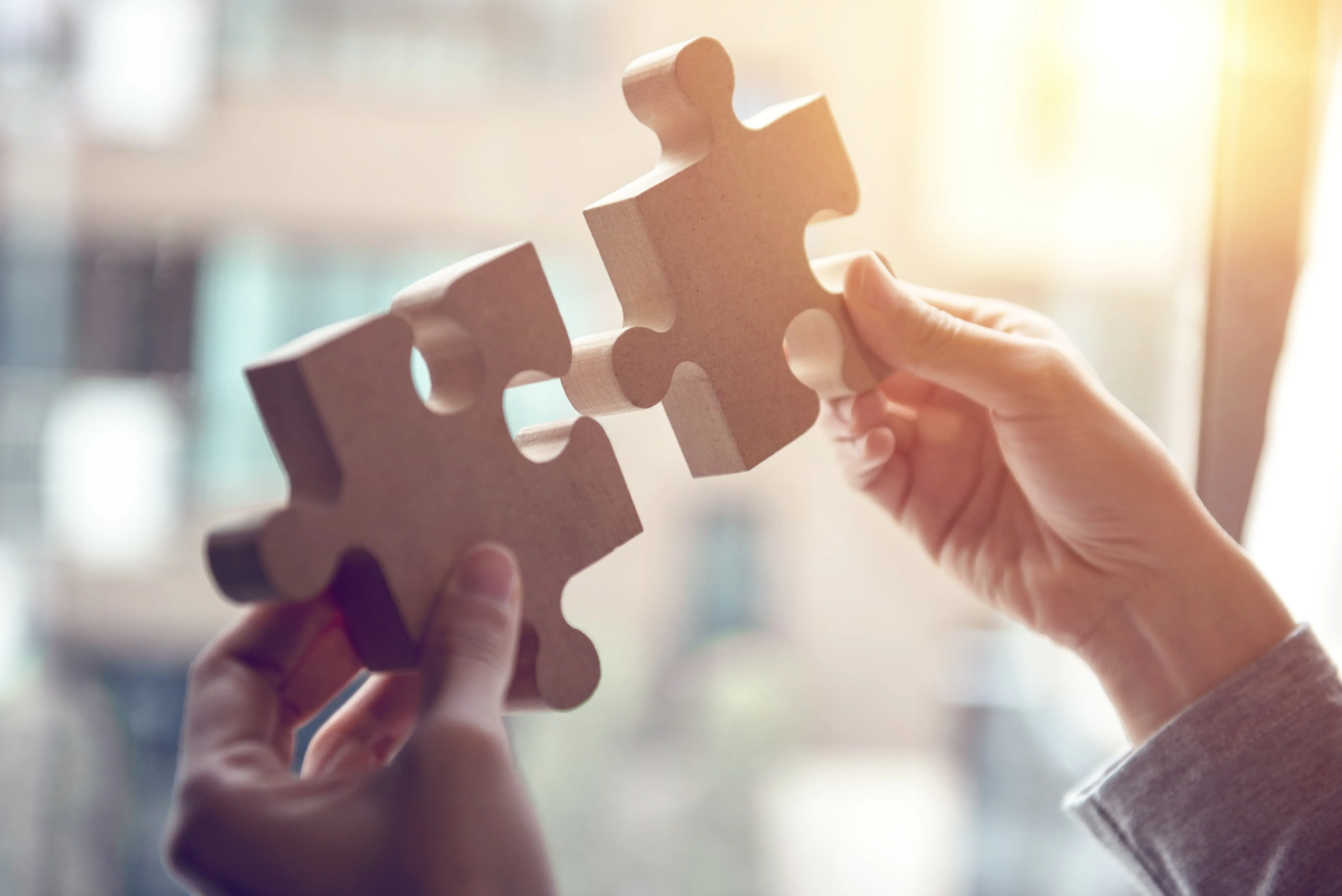 Zwei Hände halten jeweils ein Puzzlestück und fügen sie zusammen.